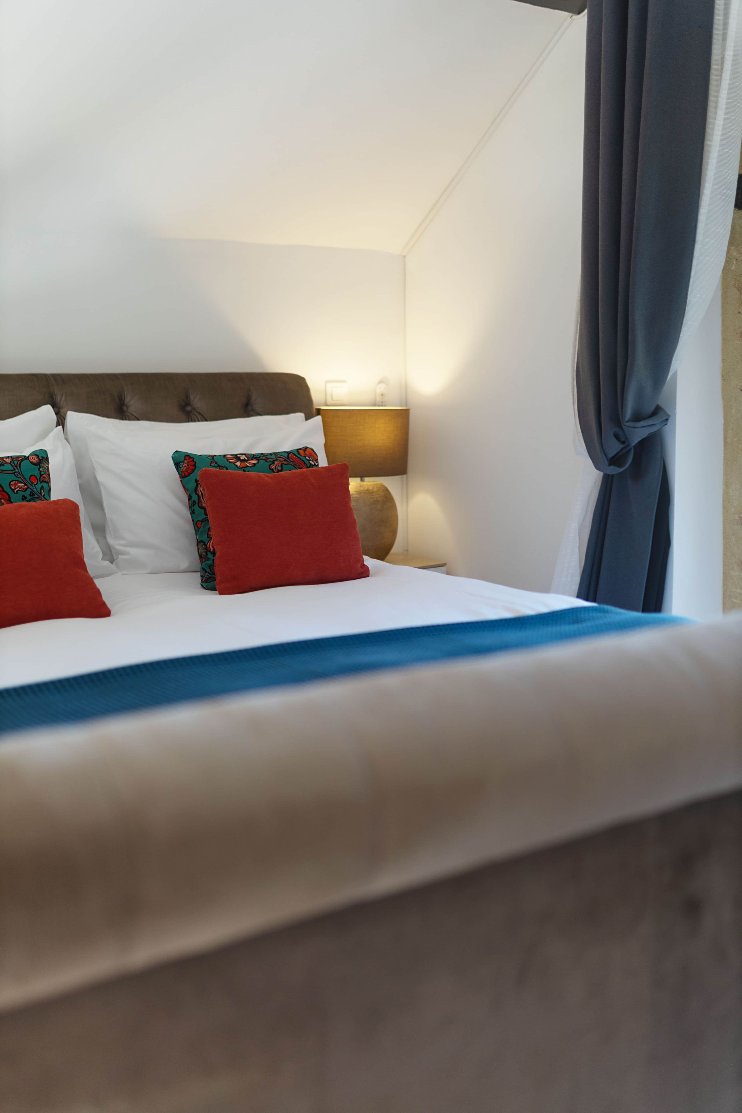 A neatly made bed with white and red pillows, a blue bedspread, and a brown headboard.