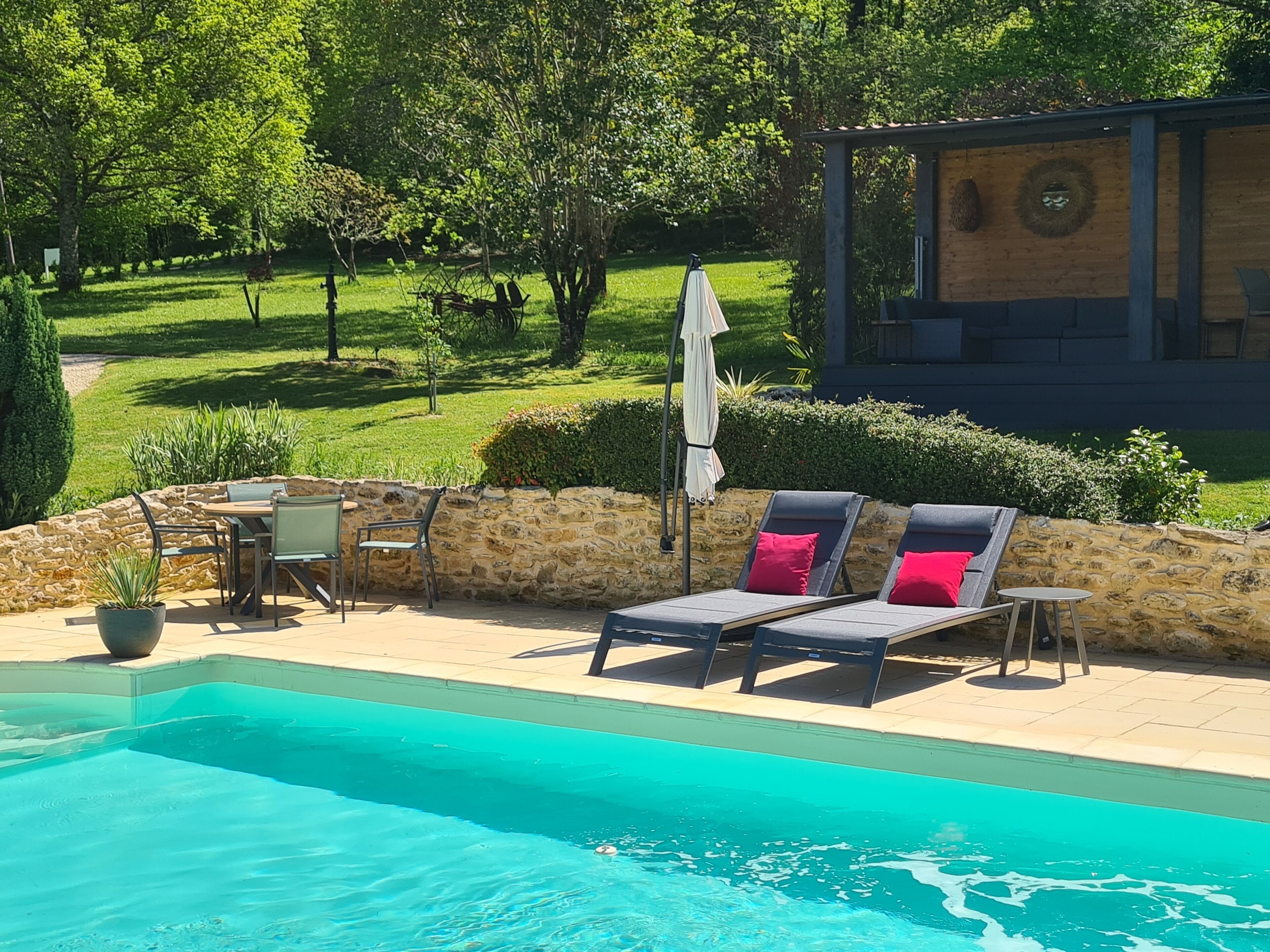 Un espace aménagé au bord de la piscine, avec des chaises longues, une table et un mur en pierre.