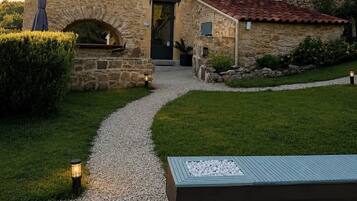 A stone building with a gravel path leading to the entrance, surrounded by a well-maintained lawn and a small garden area.
