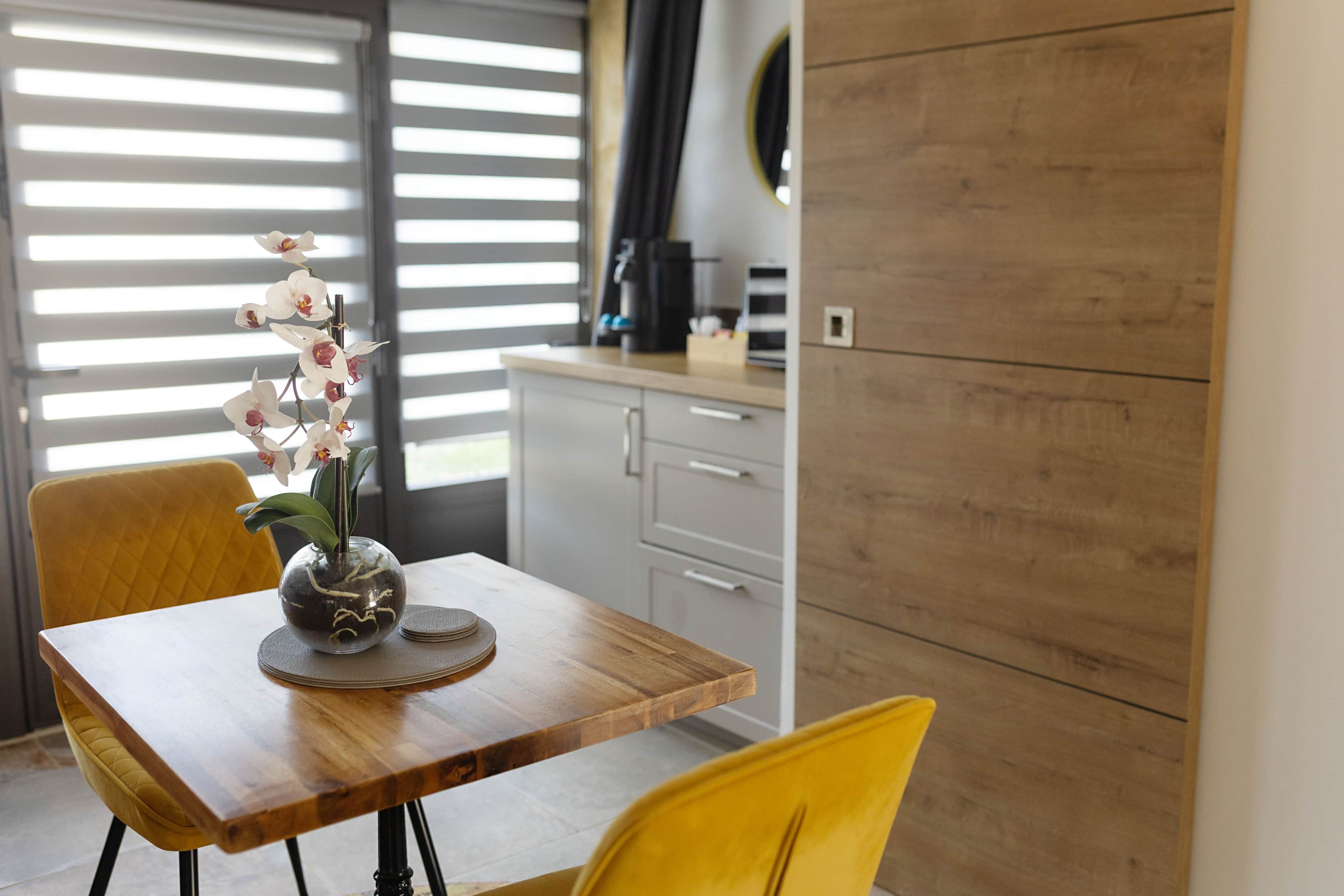 Une cuisine moderne avec une table en bois, un vase rempli de fleurs et une chaise jaune.