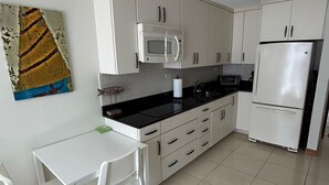 A compact kitchen with white cabinets, a microwave, a refrigerator, and a dining table with chairs. - Best Beach Location in Isla Verde, Beach Front Building! (Carolina)