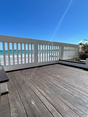 Eine Holzterrasse mit weißer Reling mit Blick auf einen Strand.