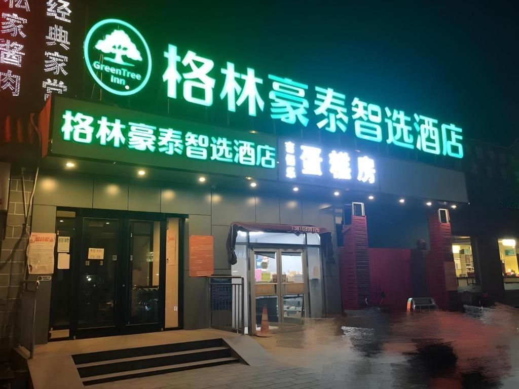 A hotel entrance with a neon sign, glass doors, and a wet ground.