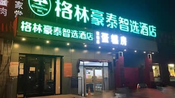 A hotel entrance with a neon sign, glass doors, and a wet ground.