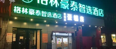 A hotel entrance with a neon sign, glass doors, and a wet ground.