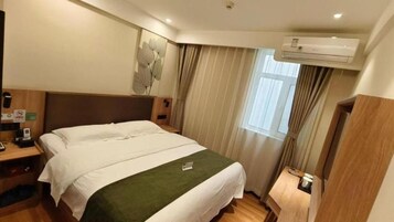 Una habitación de hotel con una cama doble, una mesita de noche, un espejo, una ventana con cortinas y un equipo de aire acondicionado.