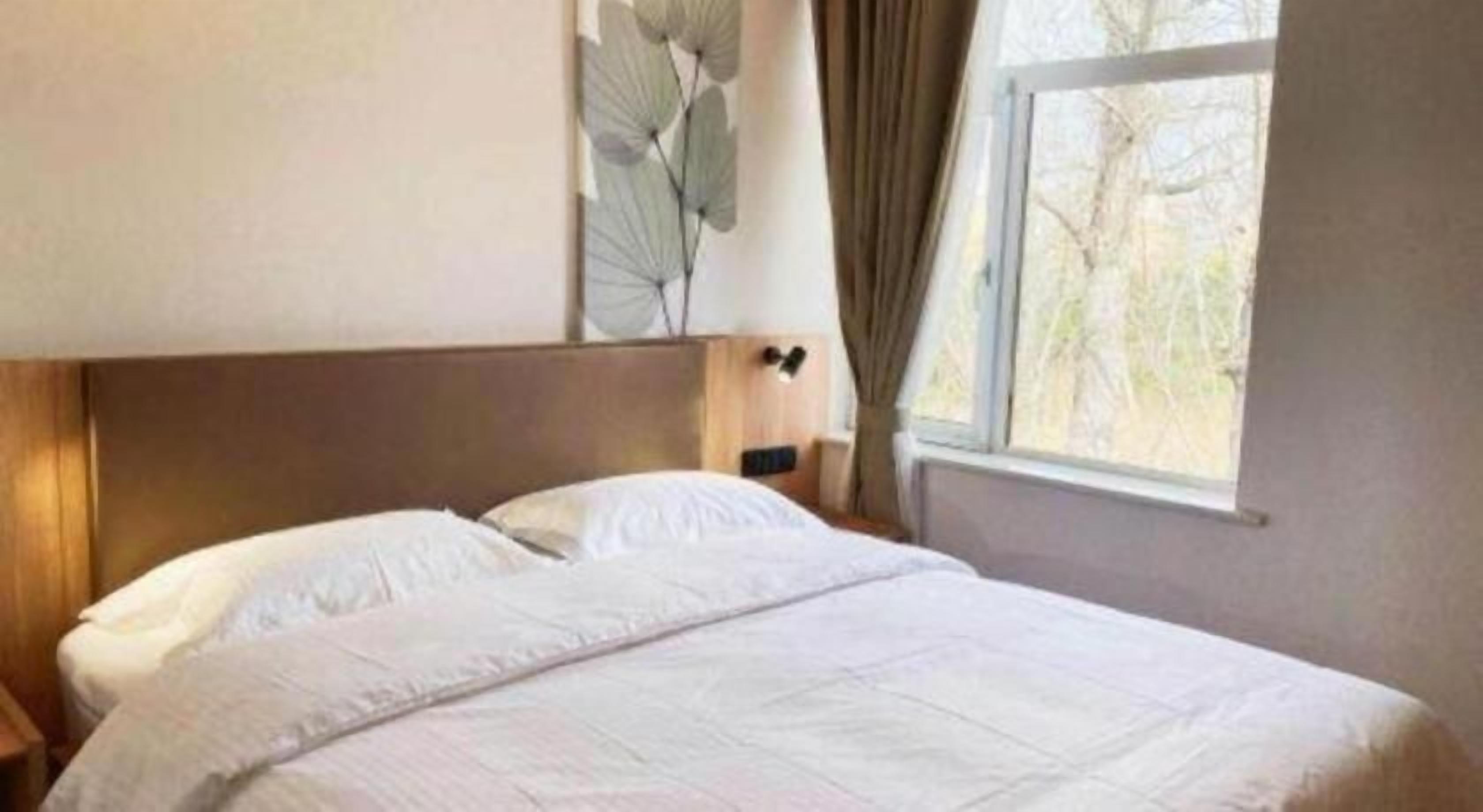 Een hotelkamer met een bed, nachtkastje, lamp en raam met gordijnen.