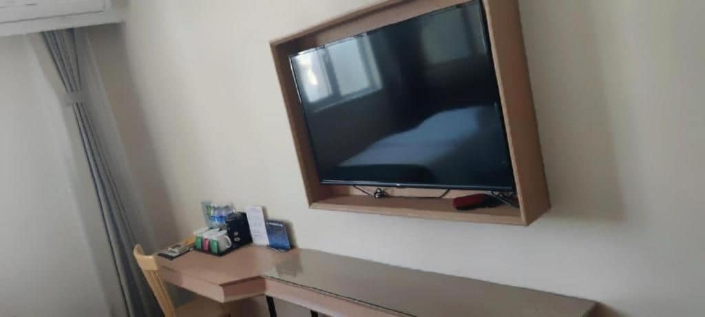 A room with a television mounted on the wall, a desk with a chair, and a window with curtains.