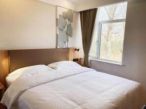 A hotel room with a large bed, a headboard, a nightstand, a wall-mounted lamp, and a window with curtains. - Greentree Inn Beijing Fangshan District Doudian Road Jinxin Yuan Express Hotel (Fangshan)