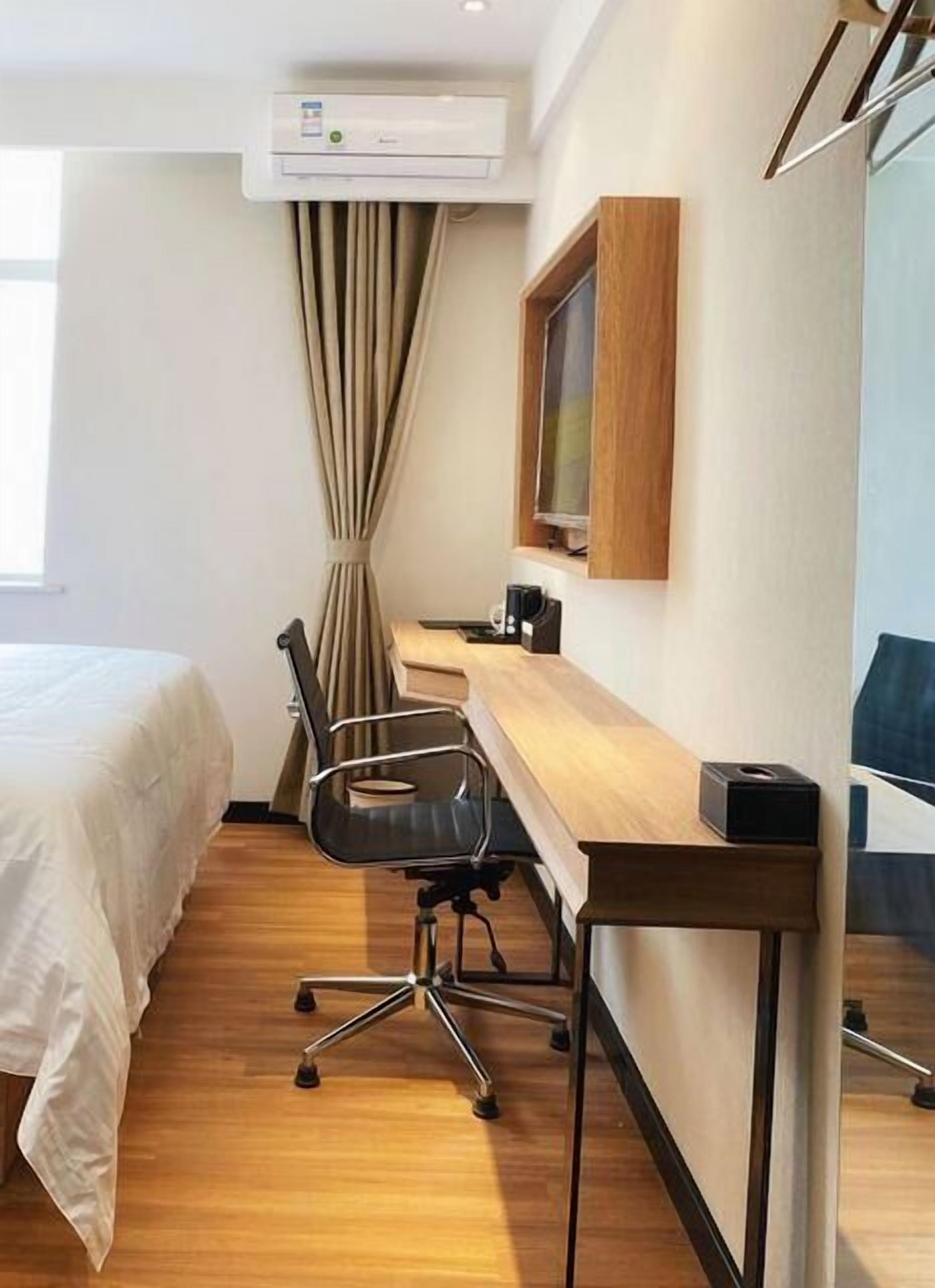 A hotel room with a bed, a desk, a chair, an air conditioner, and a window with curtains.