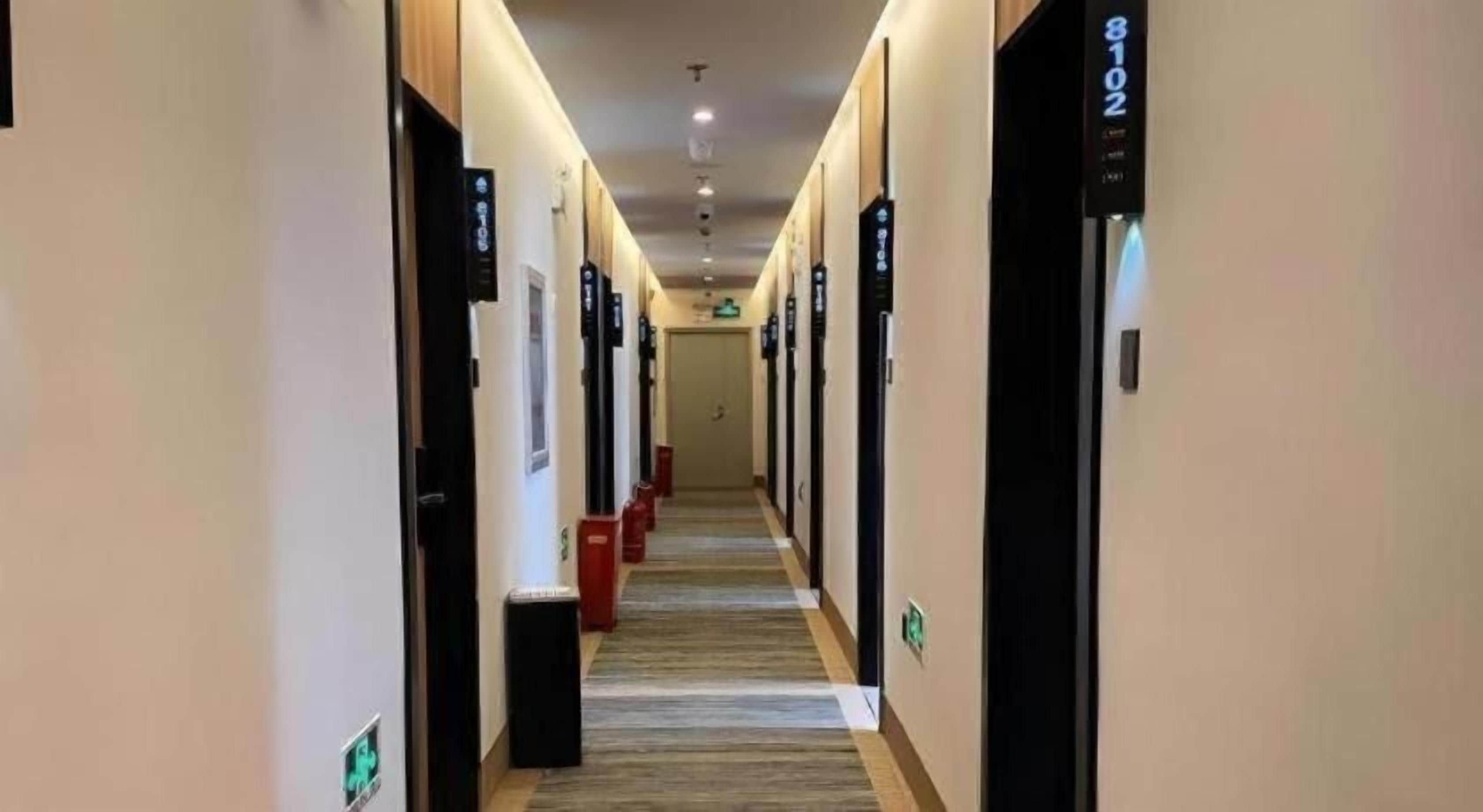 A hotel corridor with doors labeled with room numbers, a carpeted floor, and a trash bin.