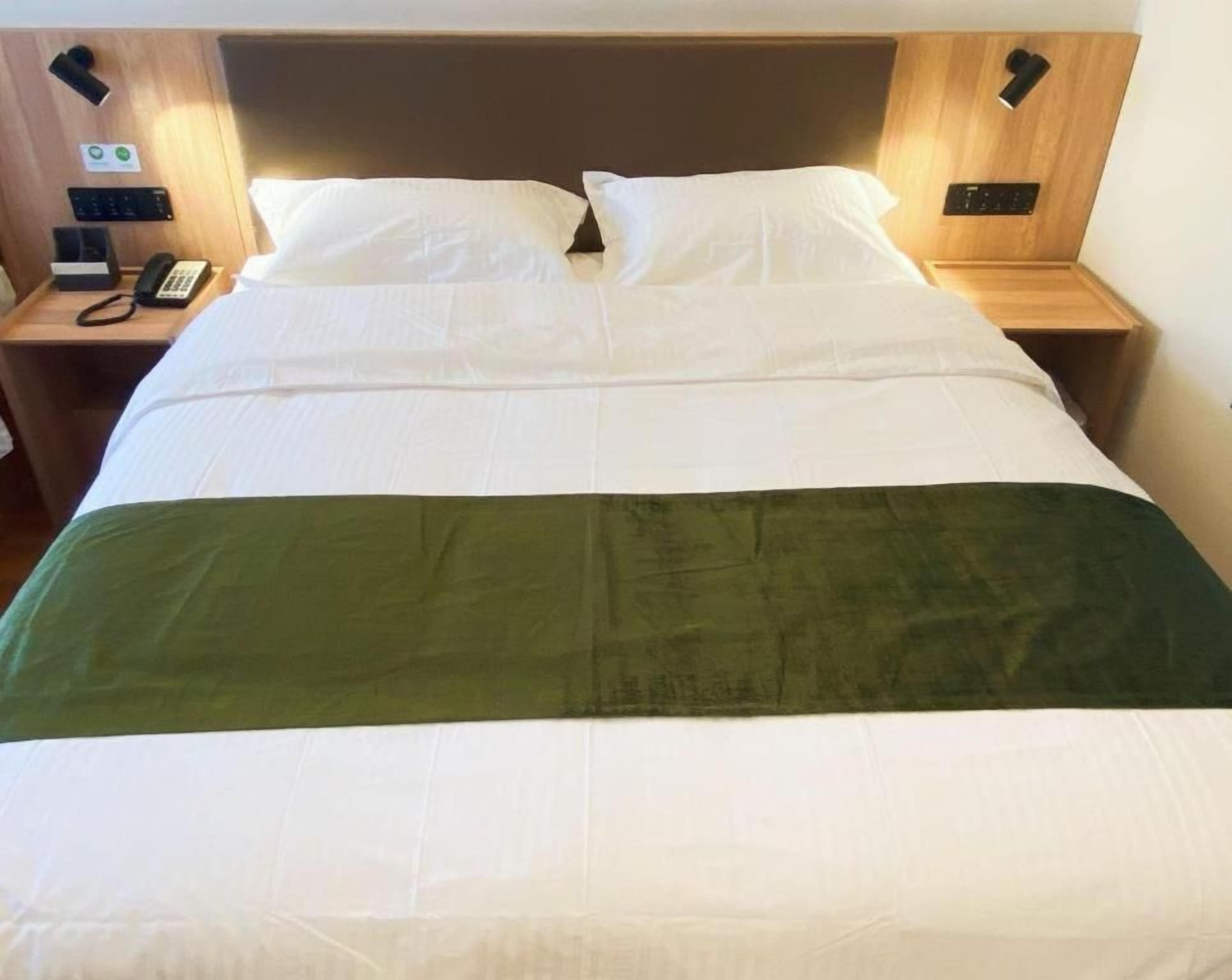 A hotel room with a bed, two bedside tables, a telephone, and a wall-mounted control panel.