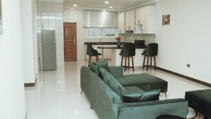 Un salon moderne avec un canapé d’angle vert, une petite table basse ronde et un coin repas avec une cuisine en arrière-plan.