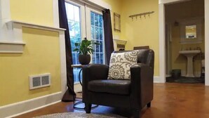A living room with a leather armchair, a potted plant, and a window with curtains. - Charming, Private, Detached Studio! (Portland)