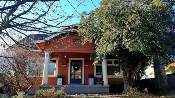 A red house with a front porch, a front door, and a large tree in front. - Charming, Private, Detached Studio! (Portland)