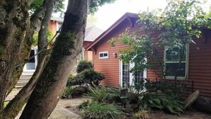 A red house with a brick pathway leading to the front door, surrounded by various plants and trees. - Charming, Private, Detached Studio! (Portland)