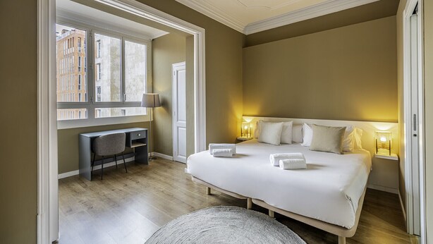 A hotel room with a bed, bedside lamps, a desk, and a chair. - Aribau D3 (Barcelona)