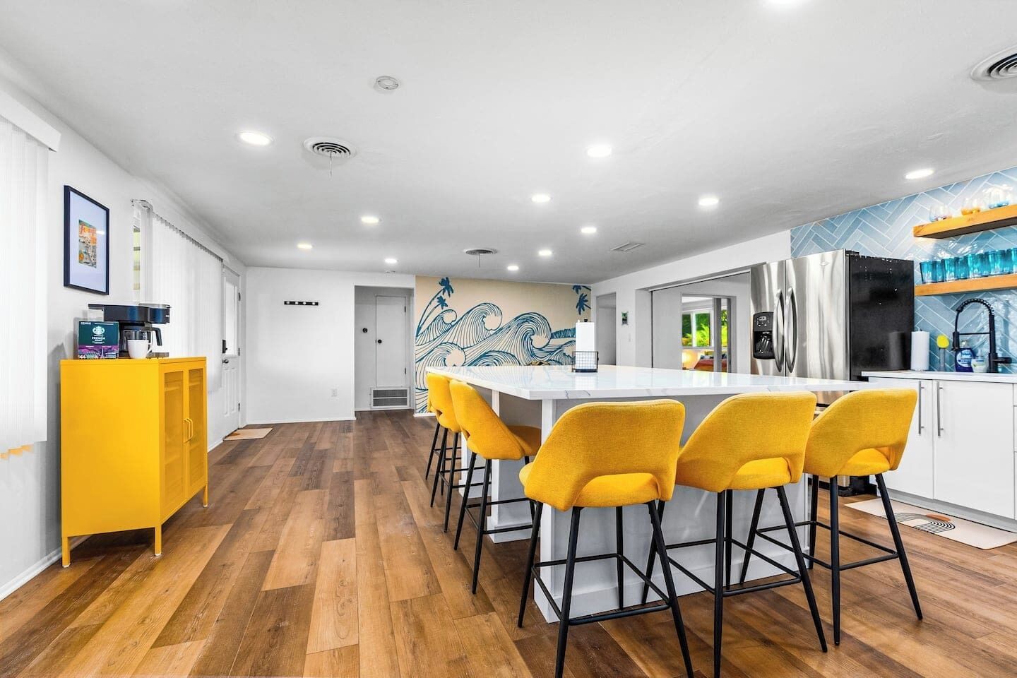 A modern kitchen with a central island, yellow bar stools, and a yellow cabinet.