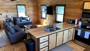 A compact cabin with a kitchenette, a sofa, a dining table, and a TV mounted on the wall.