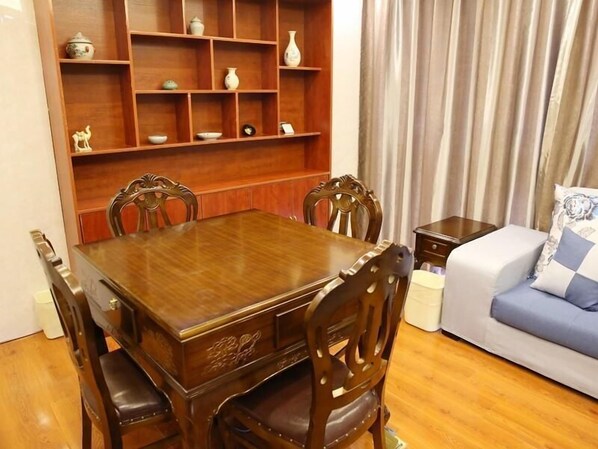 Un comedor con mesa y sillas de madera, una estantería con objetos decorativos y un sofá con cojín.