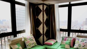 A corner sofa with green cushions and floral patterns, a black and white geometric wall panel, and a city view through large windows. - Greentree Inn Bengbu Huaiyuan County Yudu Avenue Xinhe Road Express Hotel (Bengbu)