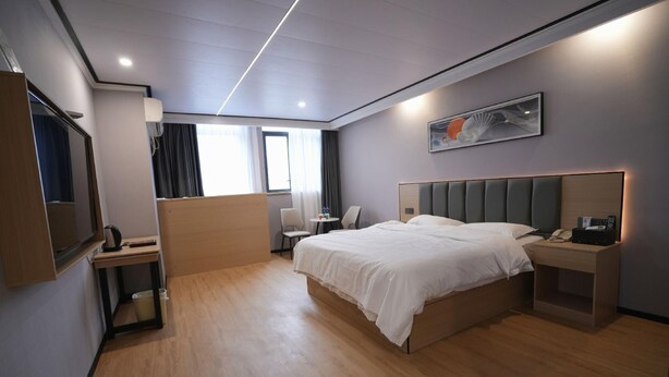 A modern hotel room with a large bed, bedside table, and a small desk with a chair. - Greentree Inn Bengbu Huaiyuan County Yudu Avenue Xinhe Road Express Hotel (Bengbu)