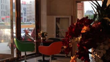 A modern interior with a large window, a green chair, a red chair, and a vase with flowers.