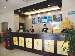 Zona de recepción de un hotel con mostrador de mármol, dos recepcionistas, una pantalla digital con información y un letrero de Wi-Fi.