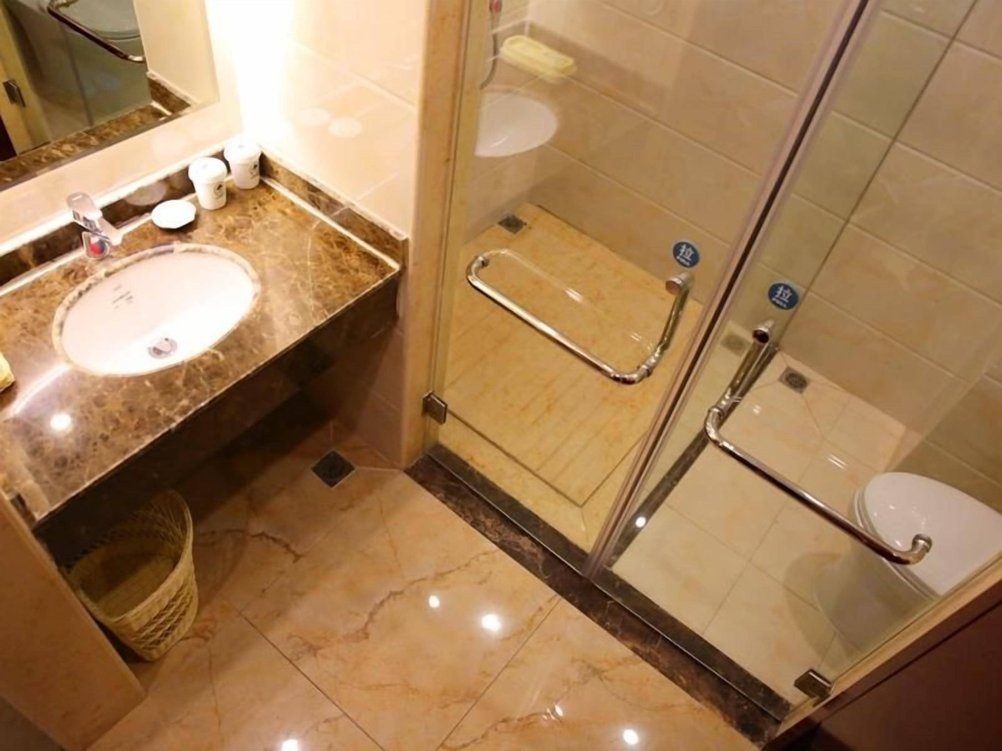 Une salle de bain avec un lavabo en marbre, une cabine de douche en verre et des toilettes blanches.