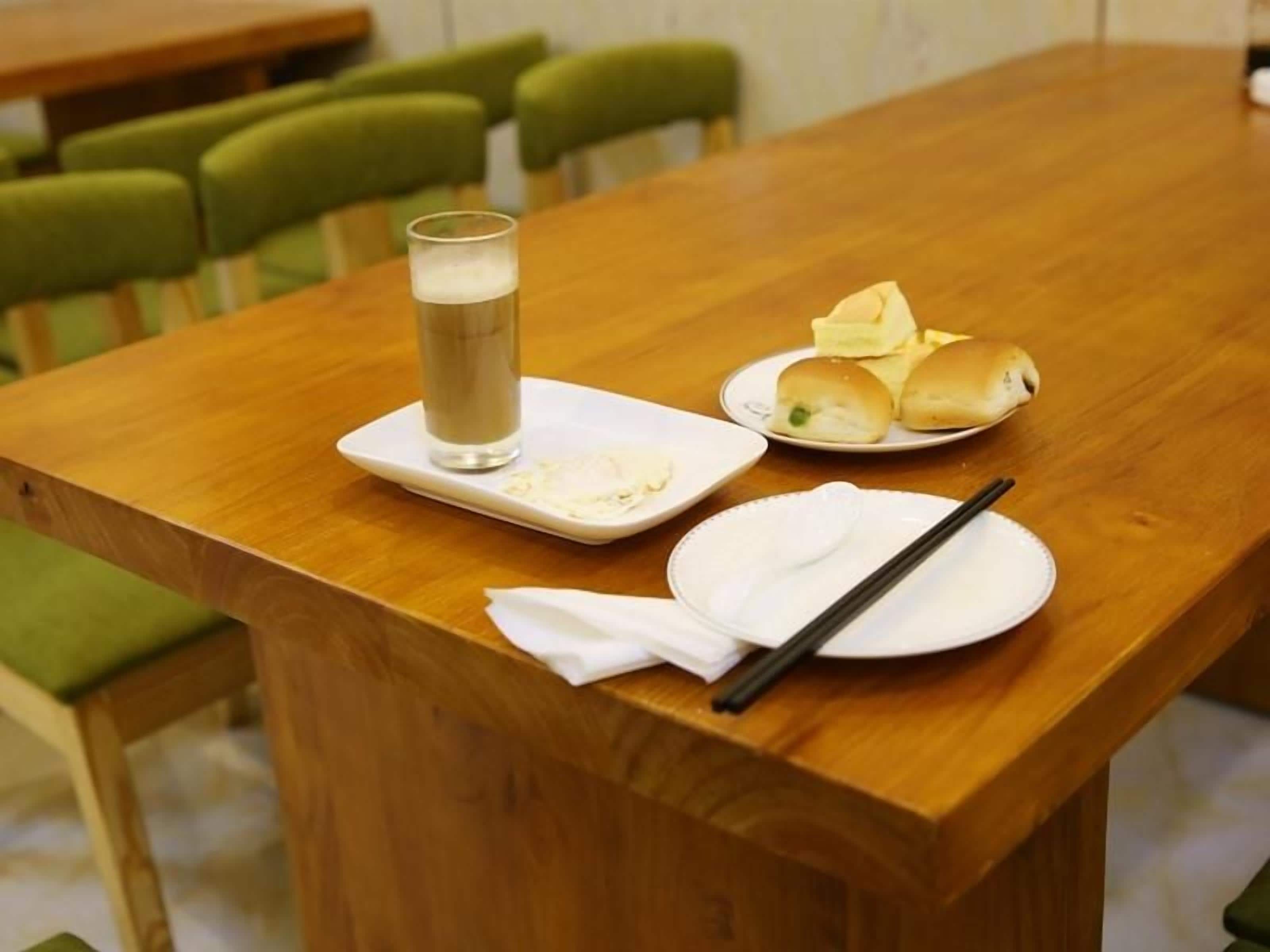 Une table en bois sur laquelle se trouvent un verre contenant une boisson claire, une assiette avec deux petits pains et une paire de baguettes posée sur une serviette.