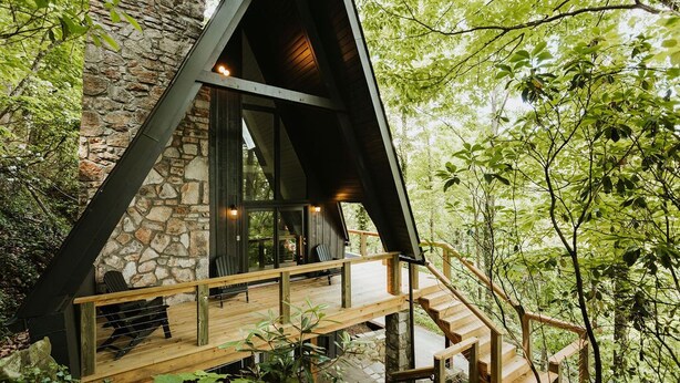 Une cabane avec une façade en pierre, une terrasse en bois et un escalier menant à un deuxième étage.