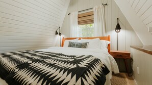 Une chambre à coucher comprenant un lit, une tête de lit en bois, deux tables de chevet, une commode, une fenêtre avec des rideaux et une lampe.