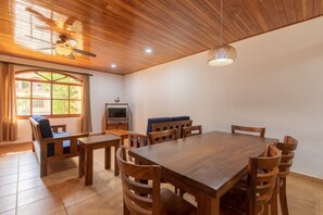 Un coin repas avec une table et des chaises en bois, un ventilateur de plafond et un téléviseur posé sur un meuble.