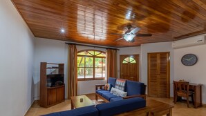 A living room with a wooden ceiling, a blue sofa, a wooden coffee table, and a television on a wooden stand. - Villa Del Sol - Deluxe Villa 2 (Nosara)