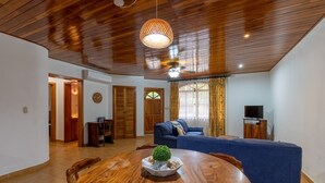 A spacious living area with a wooden dining table, blue sofa, and a television. - Villa Del Sol - Deluxe Villa 3 (Nosara)