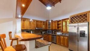 Uma cozinha com armários de madeira, geladeira de aço inoxidável, bancadas de granito e um espaço de refeições com mesa de madeira.