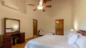 A bedroom with a bed, a wooden dresser, a mirror, a ceiling fan, and a door.