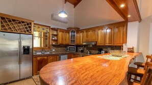 A kitchen with wooden cabinets, a stainless steel refrigerator, a granite countertop, and a large island with a woven placemat. - Villa Del Sol - Deluxe Villa 8 (Nosara)