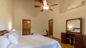A bedroom with a wooden bed, a ceiling fan, a desk with drawers, and a mirror. - Villa Del Sol - Deluxe Villa 8 (Nosara)