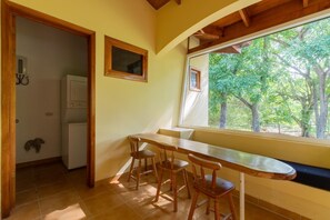 A kitchen with a built-in refrigerator, wooden chairs, and a window with a view of trees.