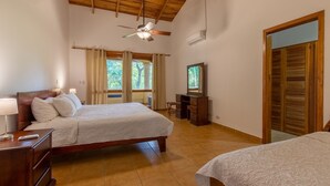 Ein Schlafzimmer mit zwei Betten, einem Schreibtisch, einem Deckenventilator und einem Fenster mit Vorhängen.