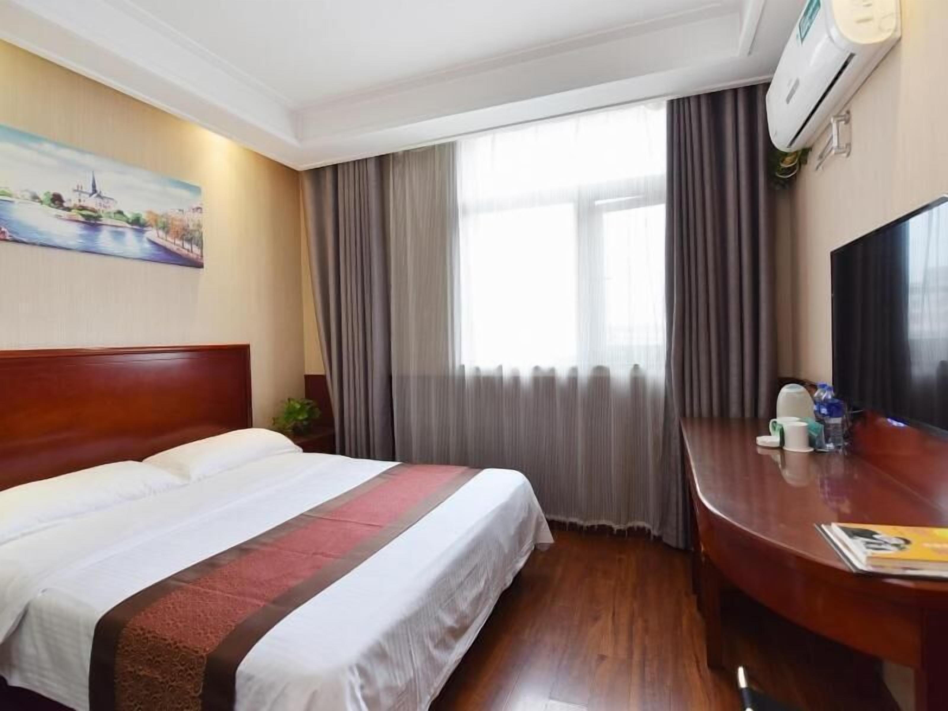 A hotel room with a bed, a desk, a TV, and a window with curtains.