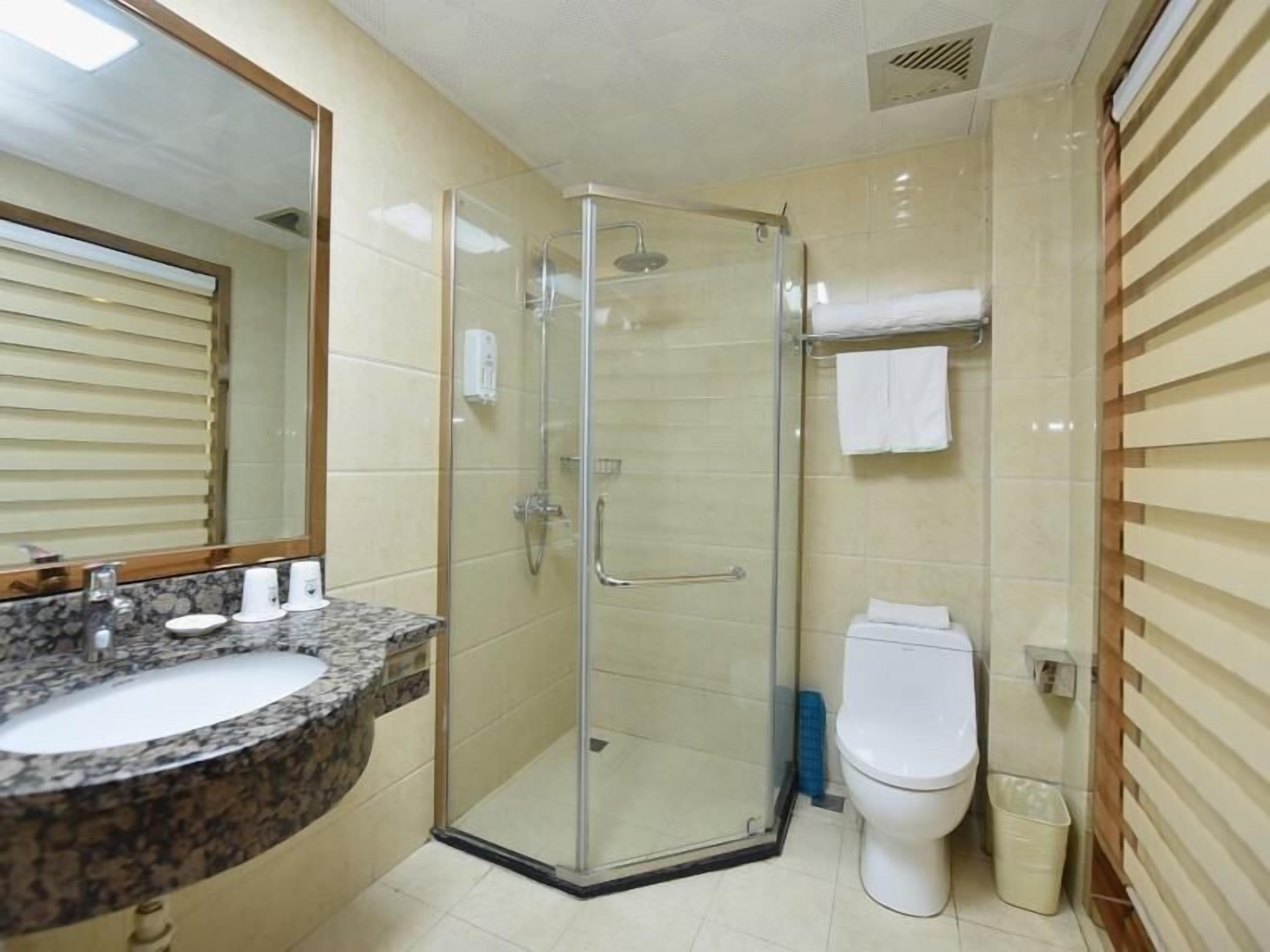 A bathroom with a glass-enclosed shower, a sink with a marble countertop, a toilet, and a mirror with a wooden frame.
