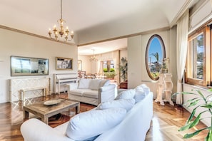 Un salón amplio con un piano, sofás blancos, una mesa de centro de madera y un espejo grande.