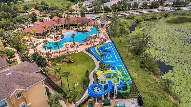 Vue aérienne d’un complexe hôtelier doté d’une piscine, d’un parc aquatique et entouré de verdure.