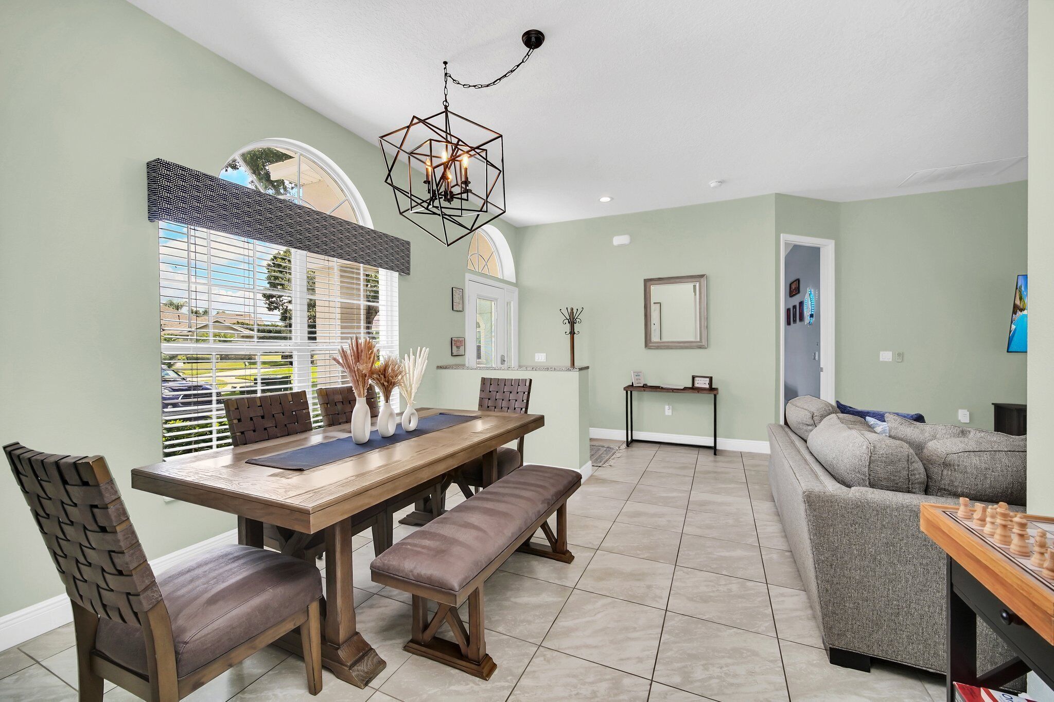 A dining area with a wooden table, chairs, and a bench. There is a chandelier above the table.