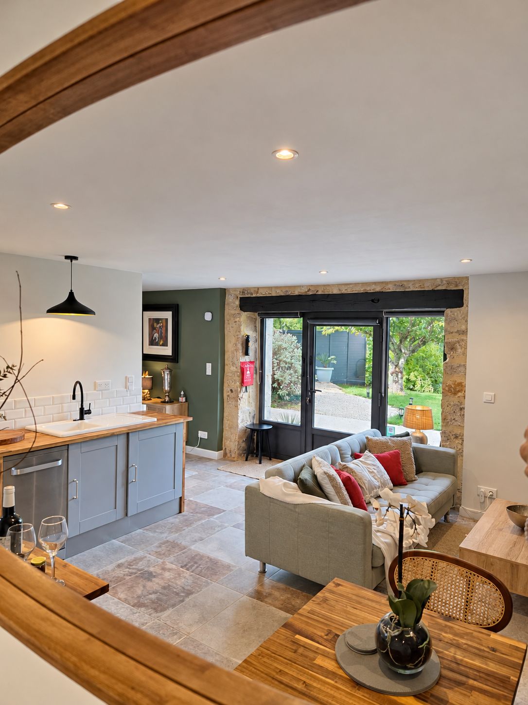 Une cuisine moderne dotée d’un four encastré, un coin repas avec une table et des chaises en bois, et un salon avec un canapé et une grande fenêtre.