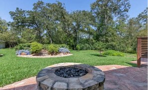 A landscaped backyard with a stone fire pit, a wooden deck, and a variety of shrubs and trees.