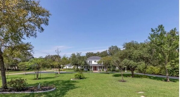 A residential property with a well-maintained lawn, mature trees, and a two-story house with a front porch.