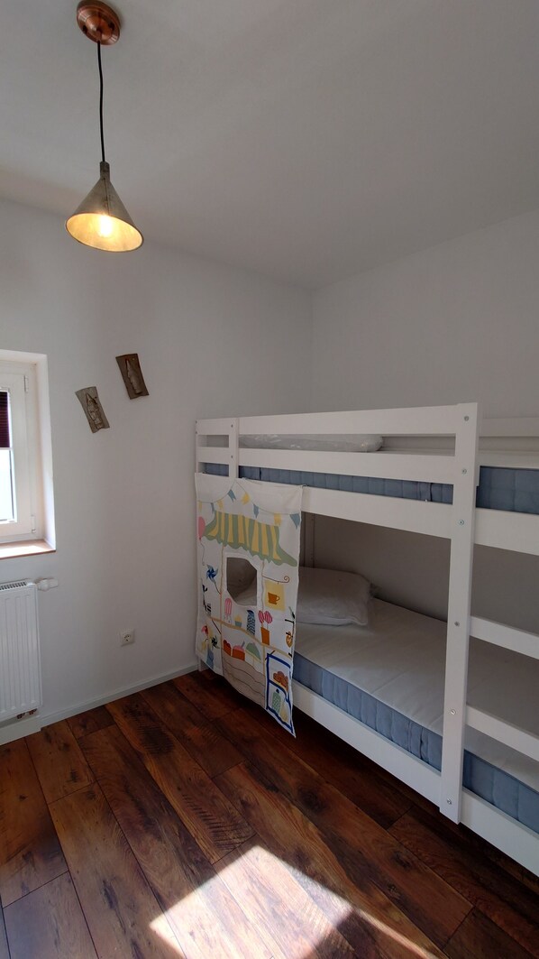 A child's bunk bed with a playhouse attached, a window with blinds, a radiator, and a hanging light fixture.